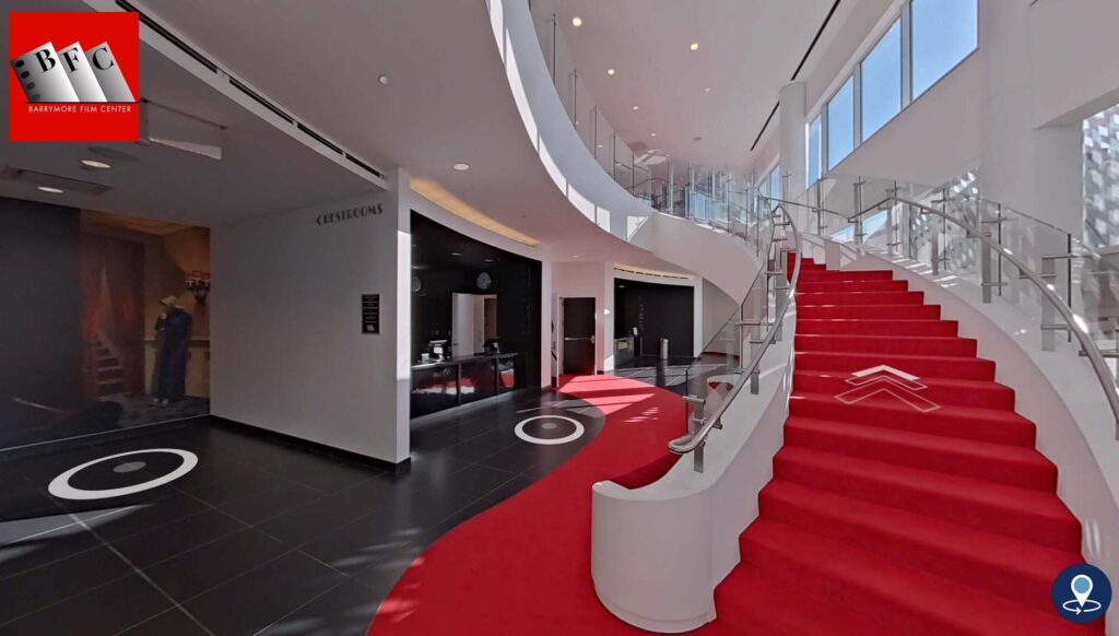 Screen grab of a virtual tour of the Barrymore Film Center witha grand staircase with red carpeting and red carpet leading towards the doors to the theater.